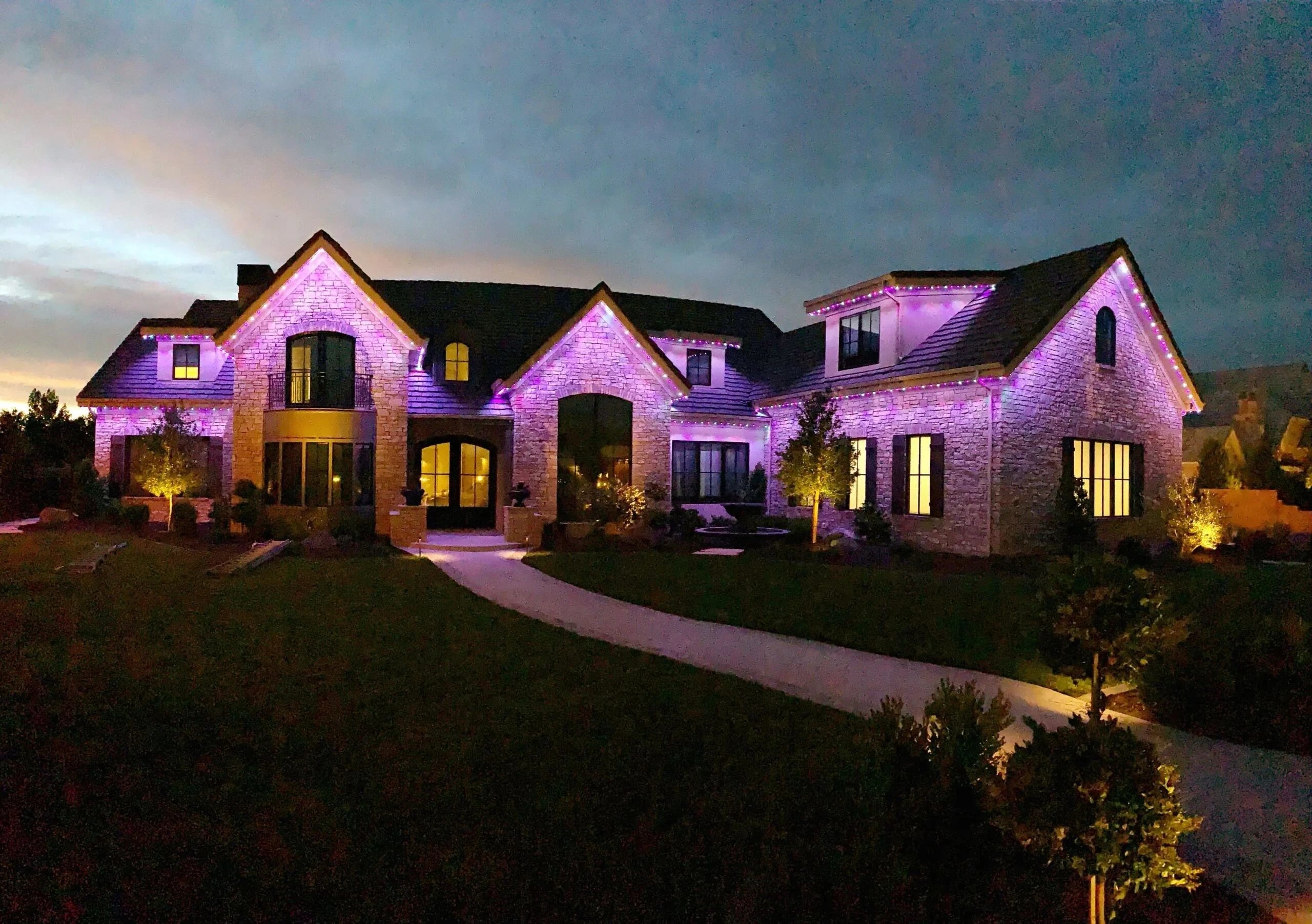 Two-story home outlined in purple permanent roofline lighting at dusk