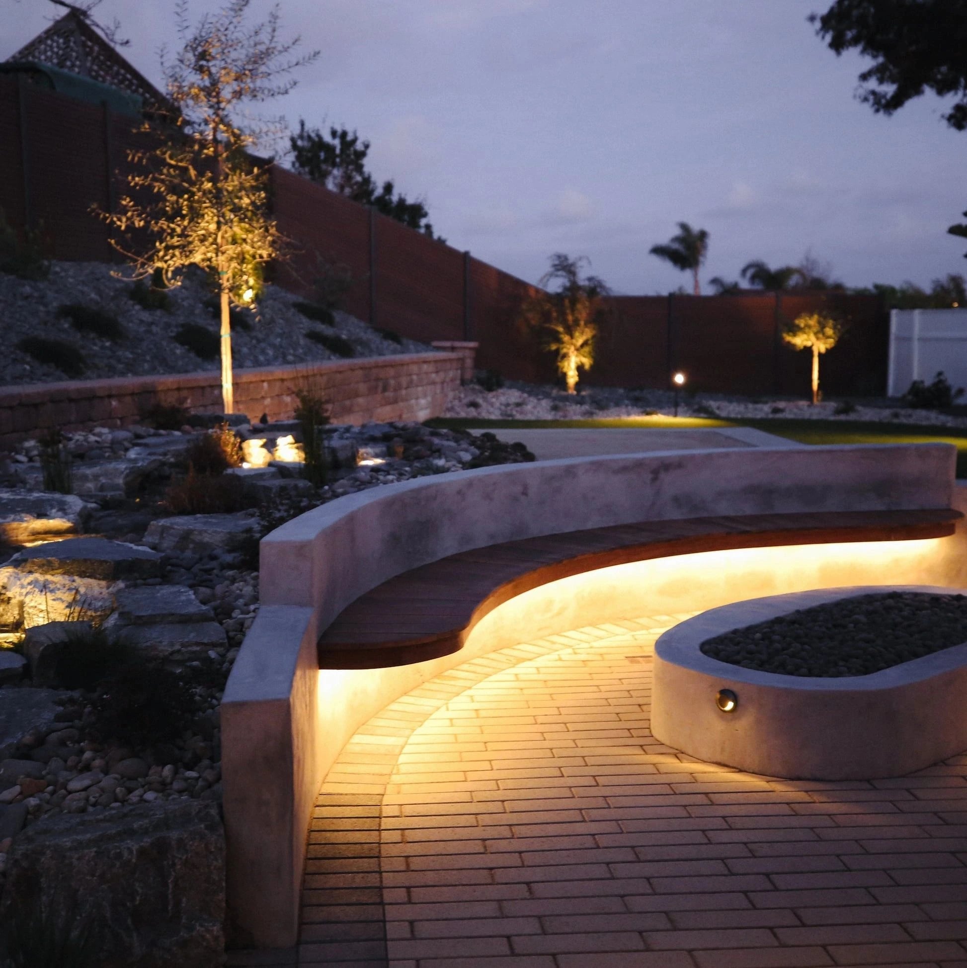 Curved concrete seat wall with LED strip lighting on a paver patio at night